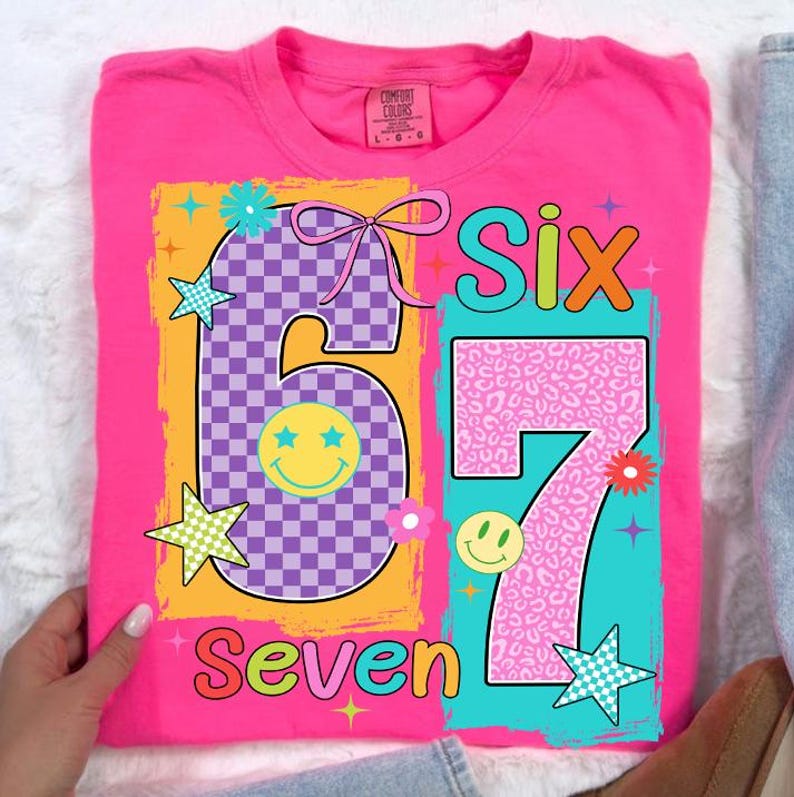 May include: A vibrant pink t-shirt featuring the numbers "6" and "7" in a playful design. The number "6" has a purple chequered pattern and a smiley face. The number "7" has a pink leopard print. The words "Six" and "Seven" are also displayed.