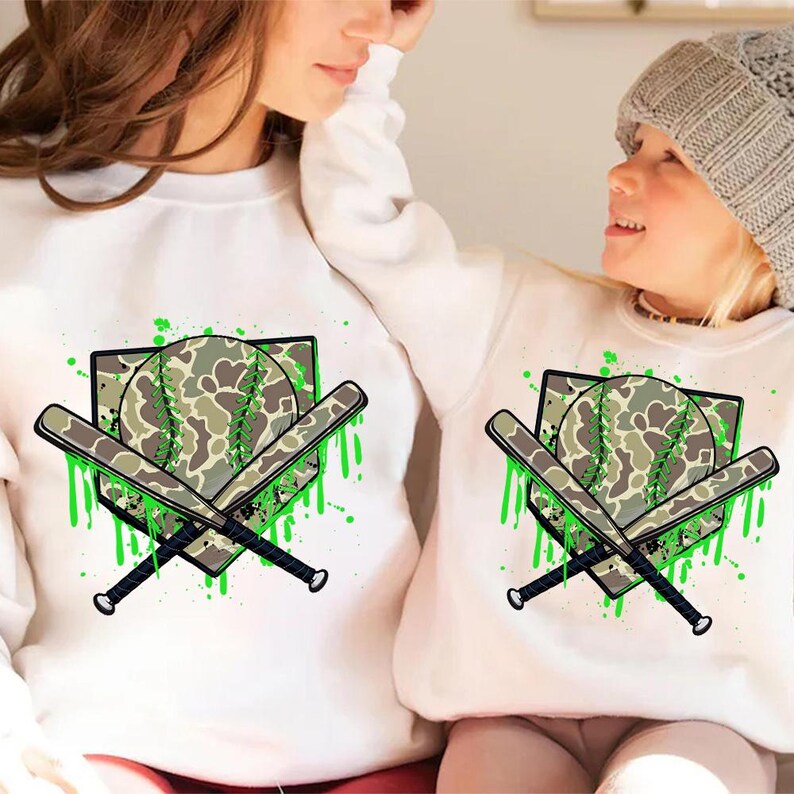May include: Matching white sweatshirts with a green and brown camouflage baseball and bats design. The design includes a home plate and green paint splatters.