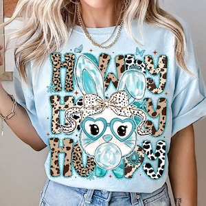 May include: Light blue t-shirt with a graphic of a bunny wearing heart-shaped glasses and a bow. The text "How Hey Hooy" is printed above and below the bunny in a mix of leopard and cow print patterns. The bunny is blowing a bubble.