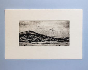 May include: A black and white etching of a mountain range with a cloudy sky. The etching is framed in a white mat.