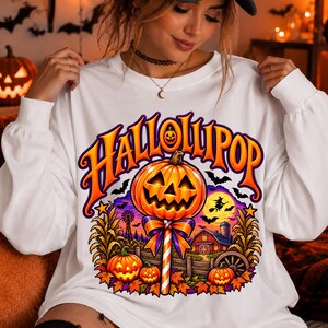 Peut inclure: Un sweat-shirt blanc à manches longues avec une impression graphique portant le texte HALLOLIPOP. Le motif comprend une grande sucette citrouille, des citrouilles plus petites, une grange rouge, des épis de maïs, des chauves-souris et une sorcière.