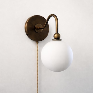 May include: A white ceramic mug with a black handle and the text "But First, Coffee" in a black, handwritten-style font. The mug is on a white surface.