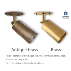May include: Two brass-colored ceiling spotlights. One is antique brass, the other is brass. The spotlights have a cylindrical shape and are mounted on a round base. The text "Antique brass" and "Brass" are below the spotlights.