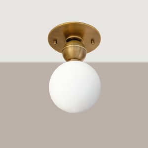 May include: A flush mount ceiling light fixture with a brass finish and a white globe shade. The fixture has a round base and a spherical glass shade. The design is simple and modern, suitable for various interior styles.