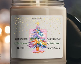 Op de afbeelding: Een brandende kaars in een glazen pot met een etiket met een kleurrijke kerstboomillustratie. Op het etiket staat "Lighting Up Christmas Nights, As Bright As Colorado Starry Skies." De kaars is van Wickly Candles.