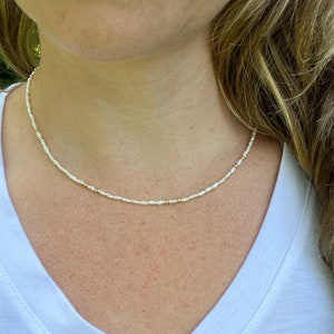 Könnte beinhalten: Eine zarte Halskette aus kleinen weißen Perlen und goldenen Perlen. Die Halskette ist schlicht und elegant und perfekt für den Alltag.
