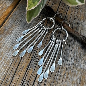 May include: Silver dangle earrings with multiple teardrop-shaped charms hanging from a circular hoop.