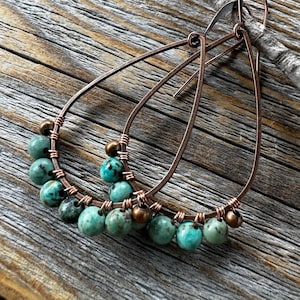 May include: Copper wire earrings with turquoise beads. The earrings are teardrop shaped and have a delicate, bohemian style.