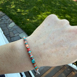 May include: A colorful beaded bracelet featuring turquoise, orange, and red disc-shaped beads. The bracelet is strung on a flexible cord and has a silver-colored clasp. The beads are approximately 0.25 inches in diameter.