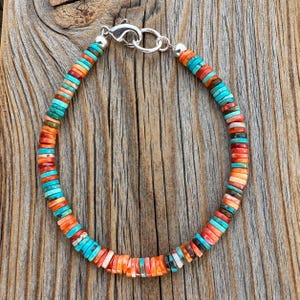 May include: A beaded bracelet featuring small, flat, disc-shaped beads in alternating shades of turquoise blue, bright orange, and coral red. The bracelet is secured with a silver-toned metal lobster claw clasp and a circular jump ring connector.