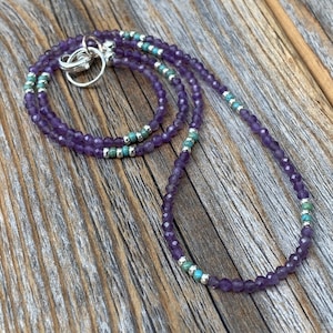 May include: A delicate necklace made with small amethyst and turquoise beads. The necklace is layered and has a silver clasp.