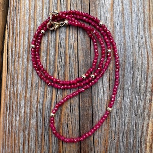 May include: A layered necklace made of small, faceted ruby red beads with gold accents.
