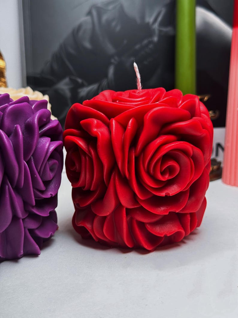 May include: Two decorative candles shaped like roses. The candle on the left is purple and the candle on the right is red.