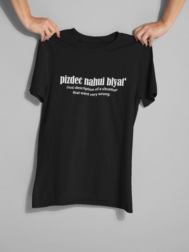 Op de afbeelding: Zwart T-shirt met witte tekst die "pizdec nahui blyat' (rus) beschrijving van een situatie die heel erg misging." zegt.