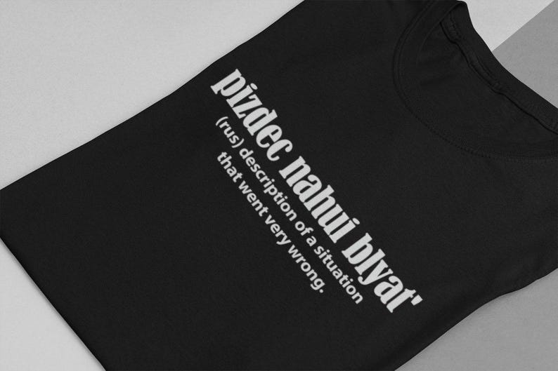 Op de afbeelding: Zwart T-shirt met witte tekst die "pizdec nahui blyat' (rus) beschrijving van een situatie die heel erg misging." zegt.