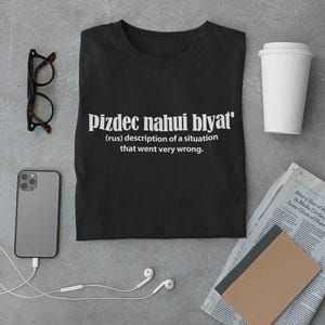 Op de afbeelding: Zwart T-shirt met witte tekst die "pizdec nahui blyat' (rus) beschrijving van een situatie die heel erg misging." luidt.