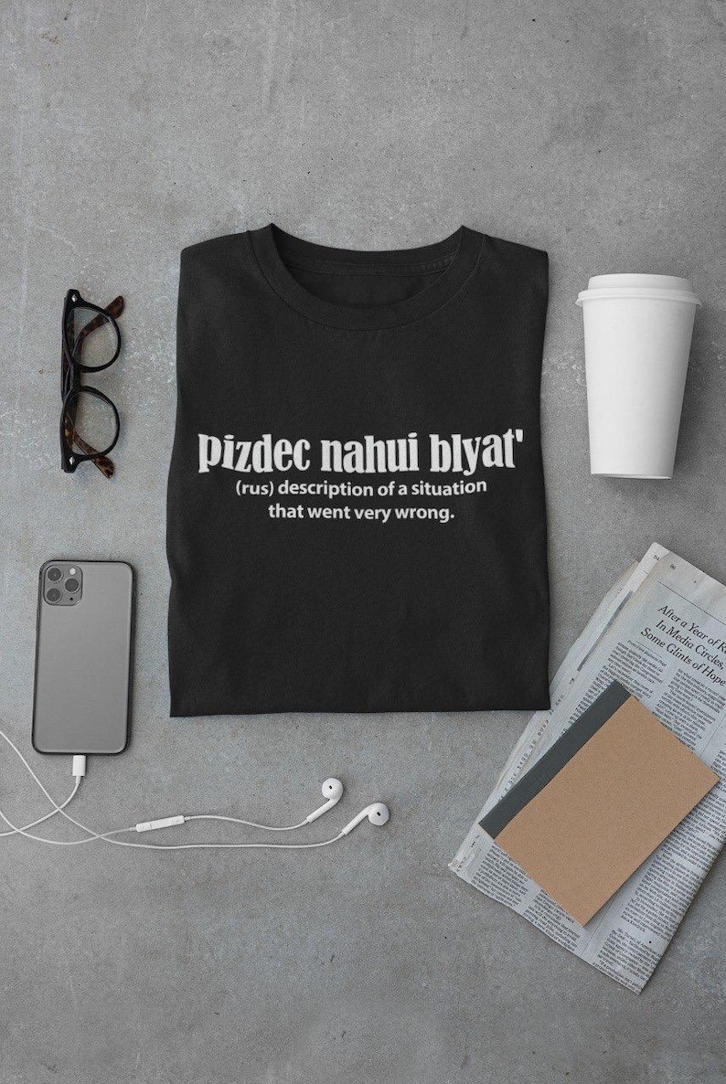Op de afbeelding: Zwart T-shirt met witte tekst die "pizdec nahui blyat' (rus) beschrijving van een situatie die heel erg misging." luidt.