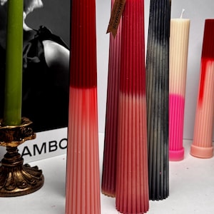 May include: Assortment of colorful, hand-made, pillar candles with a ribbed design. The candles are in shades of red, pink, black, white, and gray. The candles are arranged in a row on a white surface. The tag on one of the candles reads "Handmade".