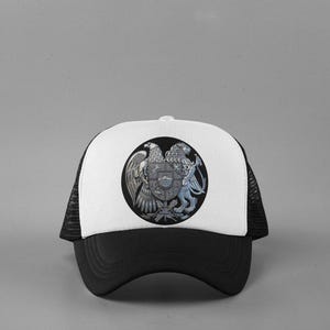 May include: A black and white trucker hat with a white front panel and a black brim. The hat features a circular emblem with a detailed design of an eagle, a lion, and a shield.