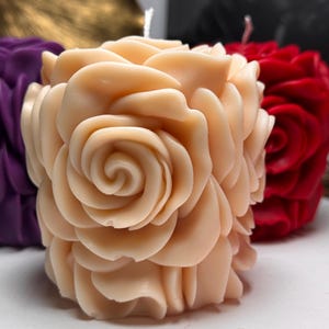 May include: A pale pink rose-shaped candle with a swirl design in the centre. The candle is made of wax and has a smooth, textured surface.