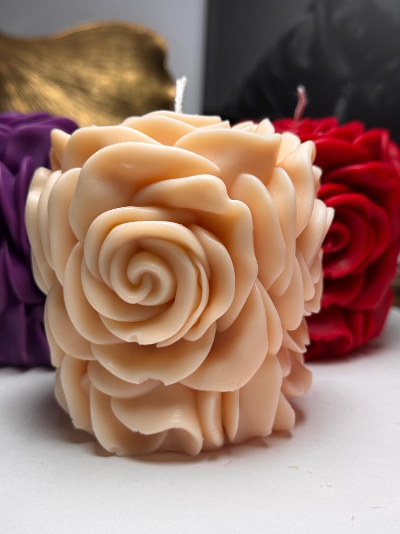 May include: A pale pink rose-shaped candle with a swirl design in the centre. The candle is made of wax and has a smooth, textured surface.