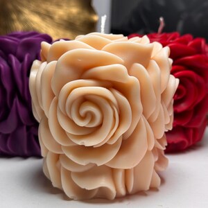 May include: A pale pink candle shaped like a rose with multiple layers of petals. The candle is on a white surface.