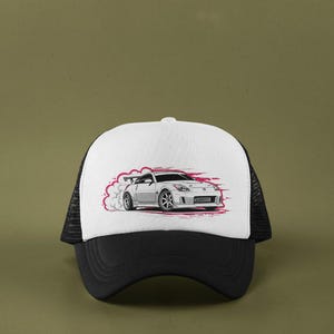 May include: A black and white trucker hat with a white front panel featuring a graphic of a white sports car with pink smoke. The hat has a black brim and mesh back.