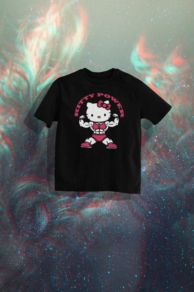 Puede incluir: Camiseta negra con un dise&ntilde;o de Hello Kitty musculosa. El dise&ntilde;o incluye el texto "KITTY POWER" en un marco circular rosa. El personaje de dibujos animados est&aacute; flexionando, con pantalones cortos rosas y un lazo.