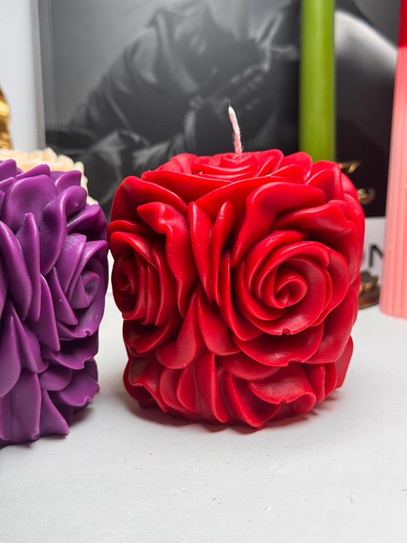 May include: Two decorative candles shaped like roses. The candle on the left is purple and the candle on the right is red.
