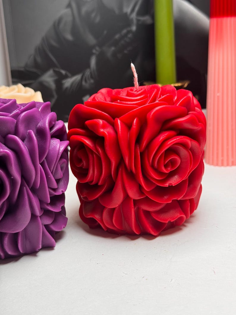 May include: Two decorative candles shaped like roses. The candle on the left is purple and the candle on the right is red.