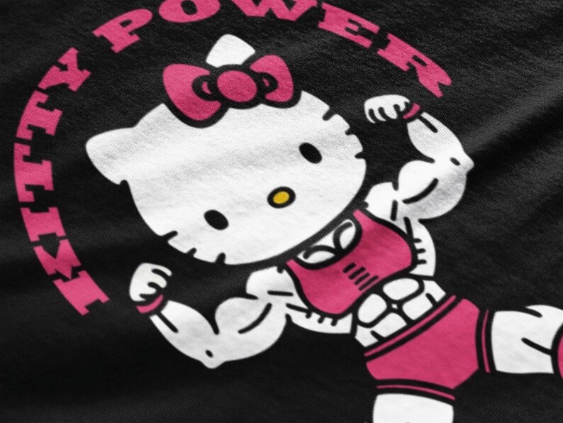 Puede incluir: Gr&aacute;fico negro con un personaje musculoso de Hello Kitty flexionando sus b&iacute;ceps. Lleva un lazo rosa, sujetador deportivo y pantalones cortos. Las palabras "KITTY POWER" est&aacute;n en rosa alrededor del personaje.
