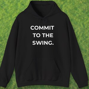 May include: Black hooded sweatshirt with a front pocket and a drawstring hood. The white text "COMMIT TO THE SWING." is printed on the front. The background is green.