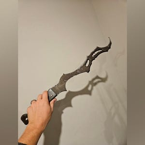 Könnte beinhalten: Ein schwarzes Metallsäbel mit einem einzigartigen, komplizierten Design. Das Säbel hat eine scharfe Spitze und eine gebogene Klinge.