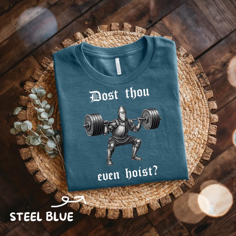 May include: Steel blue t-shirt with the text "Dost thou even hoist?" above an illustration of a knight lifting weights. The shirt is displayed on a woven basket.