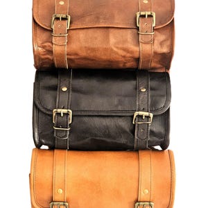 May include: Three leather bags stacked on top of each other. The top bag is brown, the middle bag is black, and the bottom bag is tan. All three bags have brass buckles and straps.