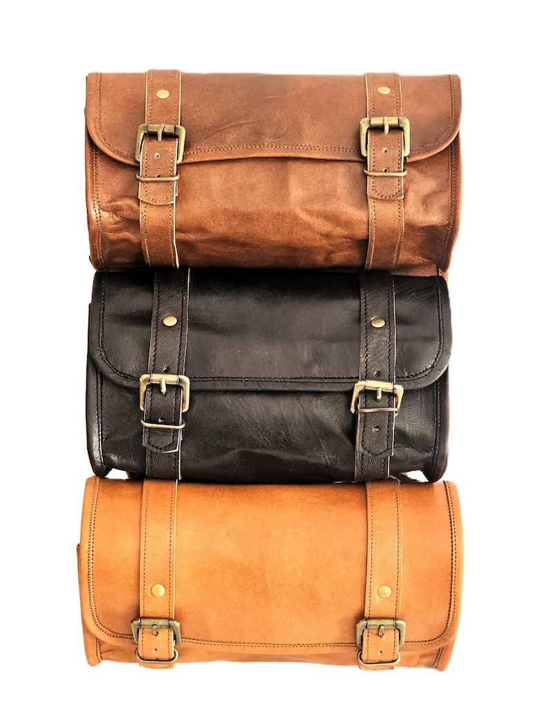 May include: Three leather bags stacked on top of each other. The top bag is brown, the middle bag is black, and the bottom bag is tan. All three bags have brass buckles and straps.