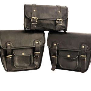 May include: Three black leather motorcycle saddlebags with brass buckles and straps. The bags are arranged in a pyramid shape, with the smallest bag on top.