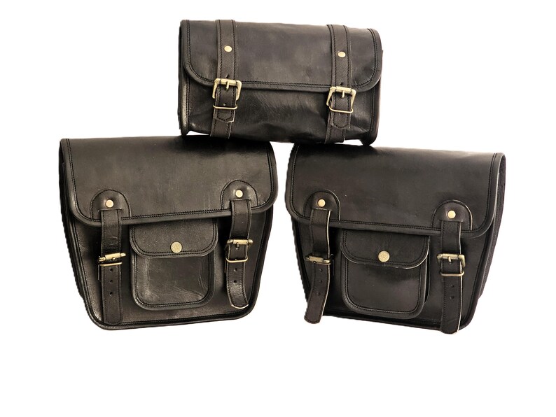 May include: Three black leather motorcycle saddlebags with brass buckles and straps. The bags are arranged in a pyramid shape, with the smallest bag on top.