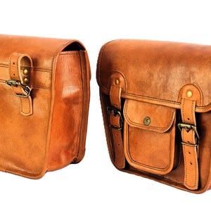 May include: Two brown leather saddlebags with buckles and straps. The bags have a flap closure and a small pocket on the front.