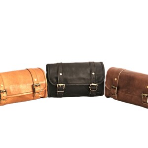 May include: Three leather motorcycle saddlebags in brown, black, and tan. Each bag has two buckles and a cylindrical shape.