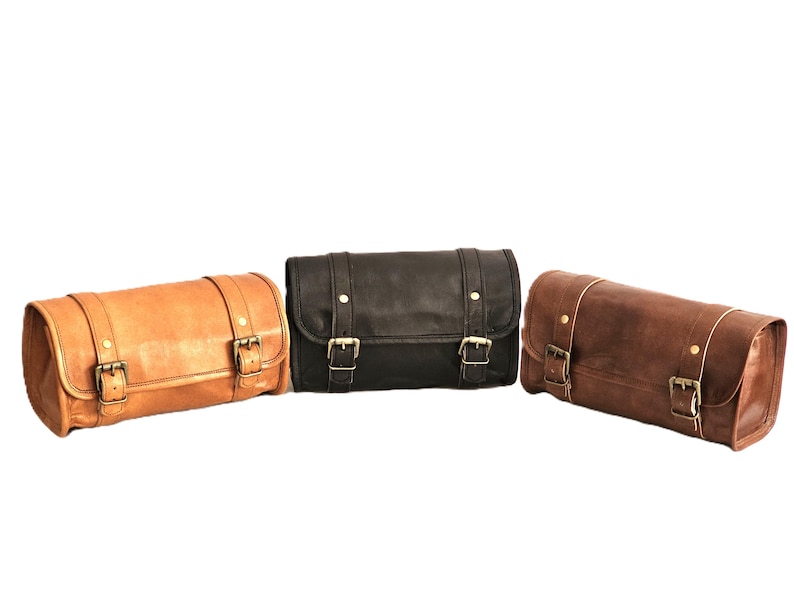 May include: Three leather motorcycle saddlebags in brown, black, and tan. Each bag has two buckles and a cylindrical shape.