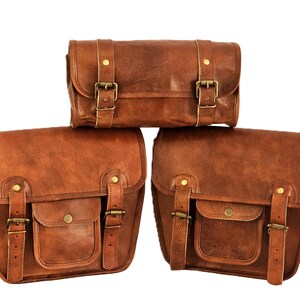 May include: Three brown leather motorcycle saddlebags with brass buckles. The bags are arranged in a pyramid shape, with the smallest bag on top and the two larger bags on the bottom.