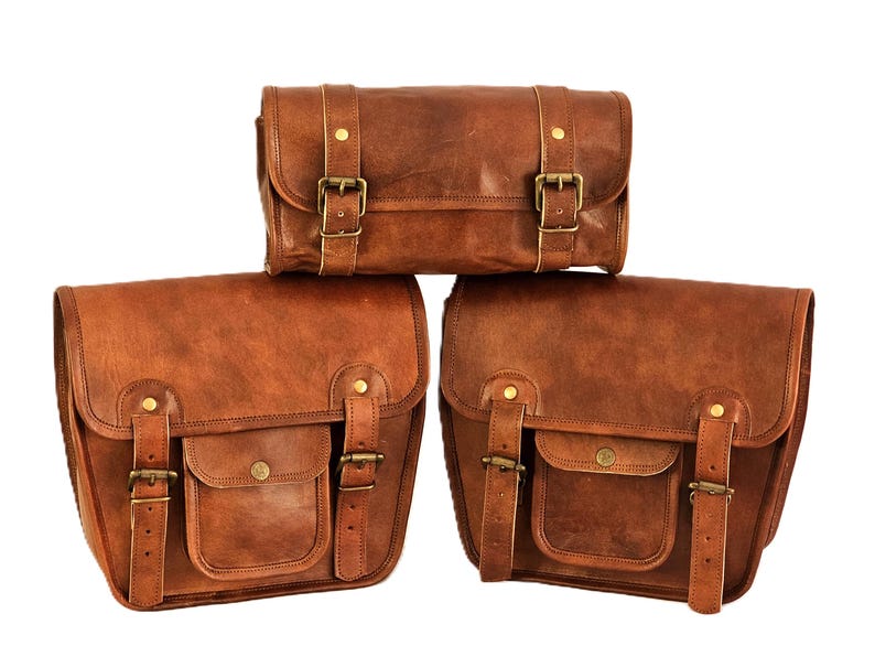 May include: Three brown leather motorcycle saddlebags with brass buckles. The bags are arranged in a pyramid shape, with the smallest bag on top and the two larger bags on the bottom.
