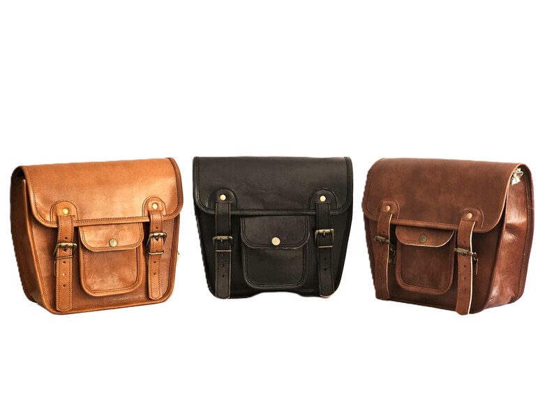 May include: Three leather motorcycle saddlebags in brown, black, and dark brown. Each bag has a flap with a buckle closure and a front pocket.