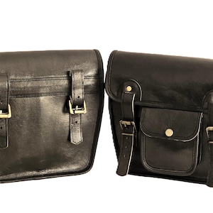 May include: Two black leather motorcycle saddlebags with buckles and straps. The saddlebags have a flap closure and a small pocket on the front.