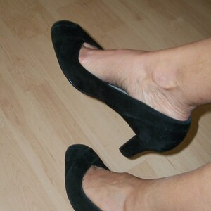 Peut inclure: Une paire de chaussures &agrave; talons en daim noir avec bout pointu. Les chaussures sont port&eacute;es sur un sol en bois.
