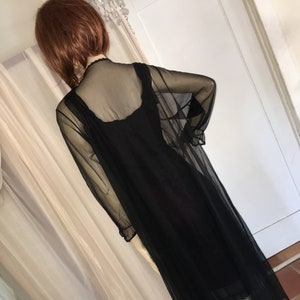 May include: A black sheer maxi dress with a long-sleeved sheer overlay. The dress has a scoop neckline and a fitted bodice. The overlay has a lace trim at the neckline and wrists.