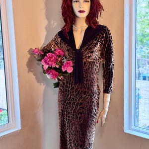 May include: A brown and black leopard print velvet dress with a black velvet collar and a bow tie. The dress has long sleeves and a fitted silhouette. The model is wearing a pearl necklace.