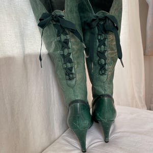 May include: A pair of green leather knee-high boots with a stiletto heel and lace-up detail on the back.