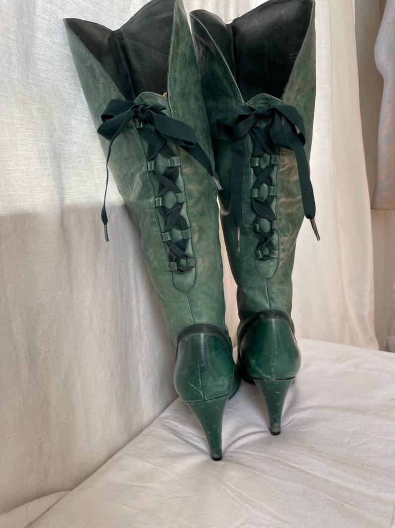 May include: A pair of green leather knee-high boots with a stiletto heel and lace-up detail on the back.